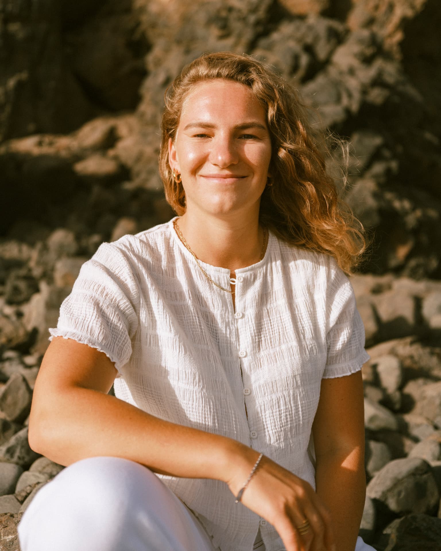 Elena sitting among volcanic rocks in warm sunlight